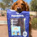 A happy dog holding a bag of the Pawstruck Beef Jerky Joint Health Treats